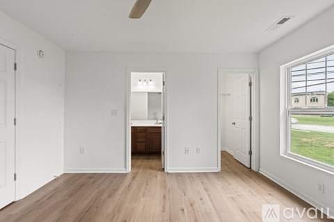 A spacious room with wooden floors and white walls, featuring a kitchenette with a sink and a window with a view of the outside.