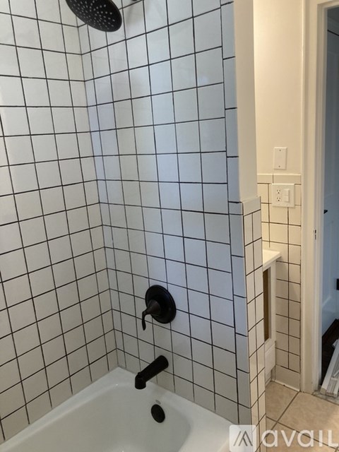 A white tiled shower with a black shower head and faucet.