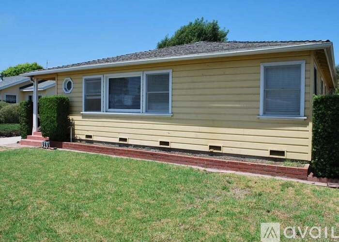 A yellow house with a red brick border around the front yard.