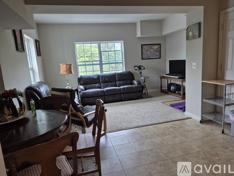 A living room with a black leather couch and a wooden dining table.