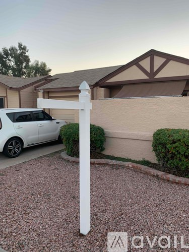 A white car is parked in front of a house with a white fence.