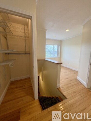 A room with a wooden floor and a white wall with a doorway leading to another room.