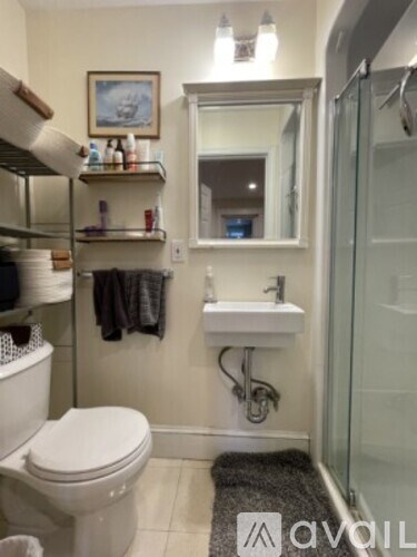 A bathroom with a toilet, sink, mirror, and shelves.