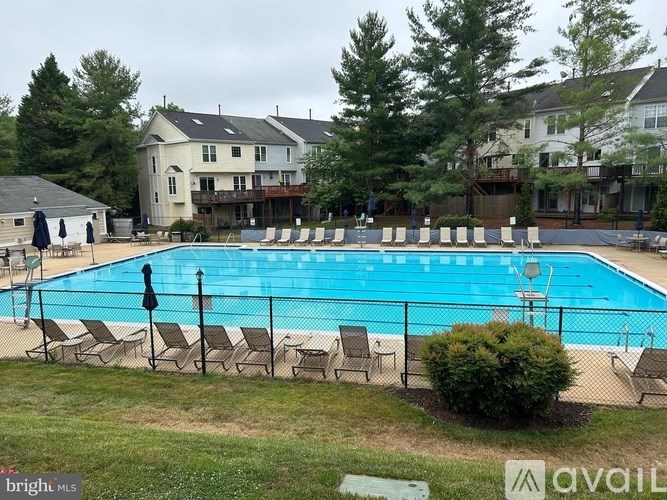 A pool surrounded by lawn chairs and trees.