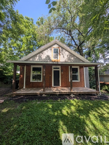 A small house with a porch is surrounded by greenery.