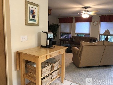 A living room with a couch, a table with a coffee maker on it, and a painting of a rooster on the wall.