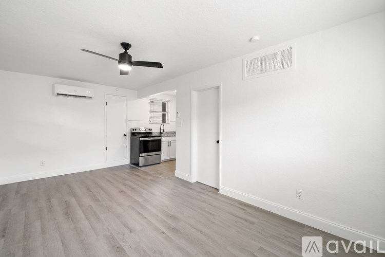 A spacious room with a ceiling fan and a kitchen area in the background.