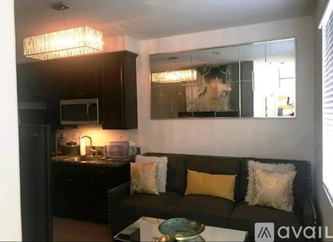 A modern living room with a black couch and a kitchen area in the background.