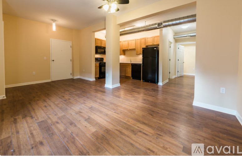 A spacious room with wooden flooring and a black refrigerator.