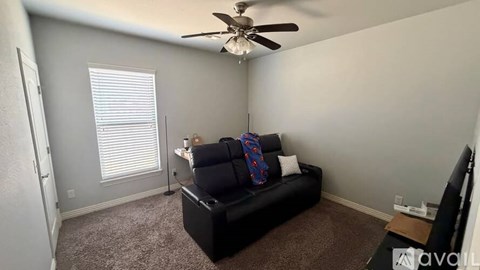 A living room with a black couch and a ceiling fan.