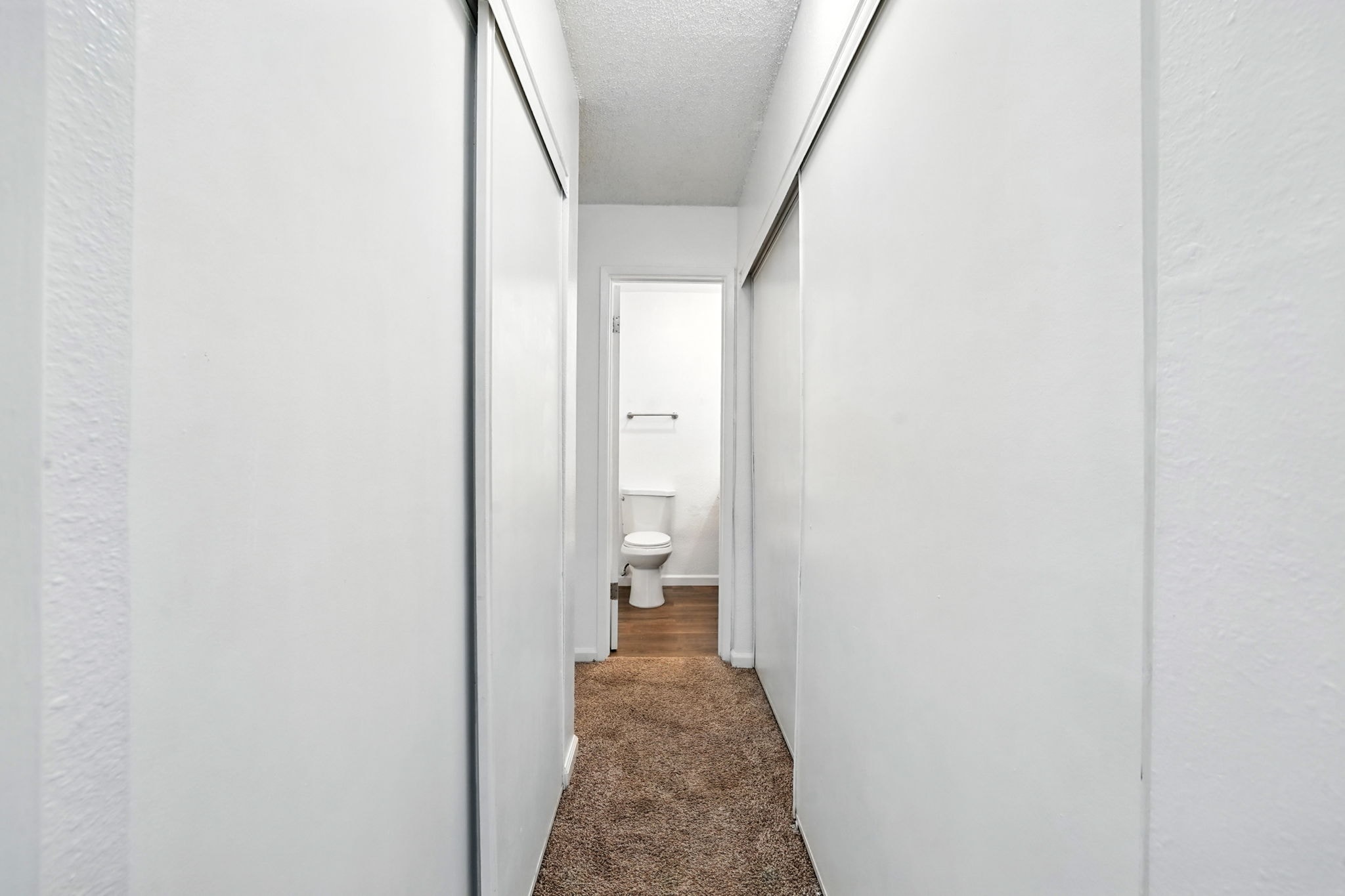 A narrow hallway with a carpeted floor and white walls.