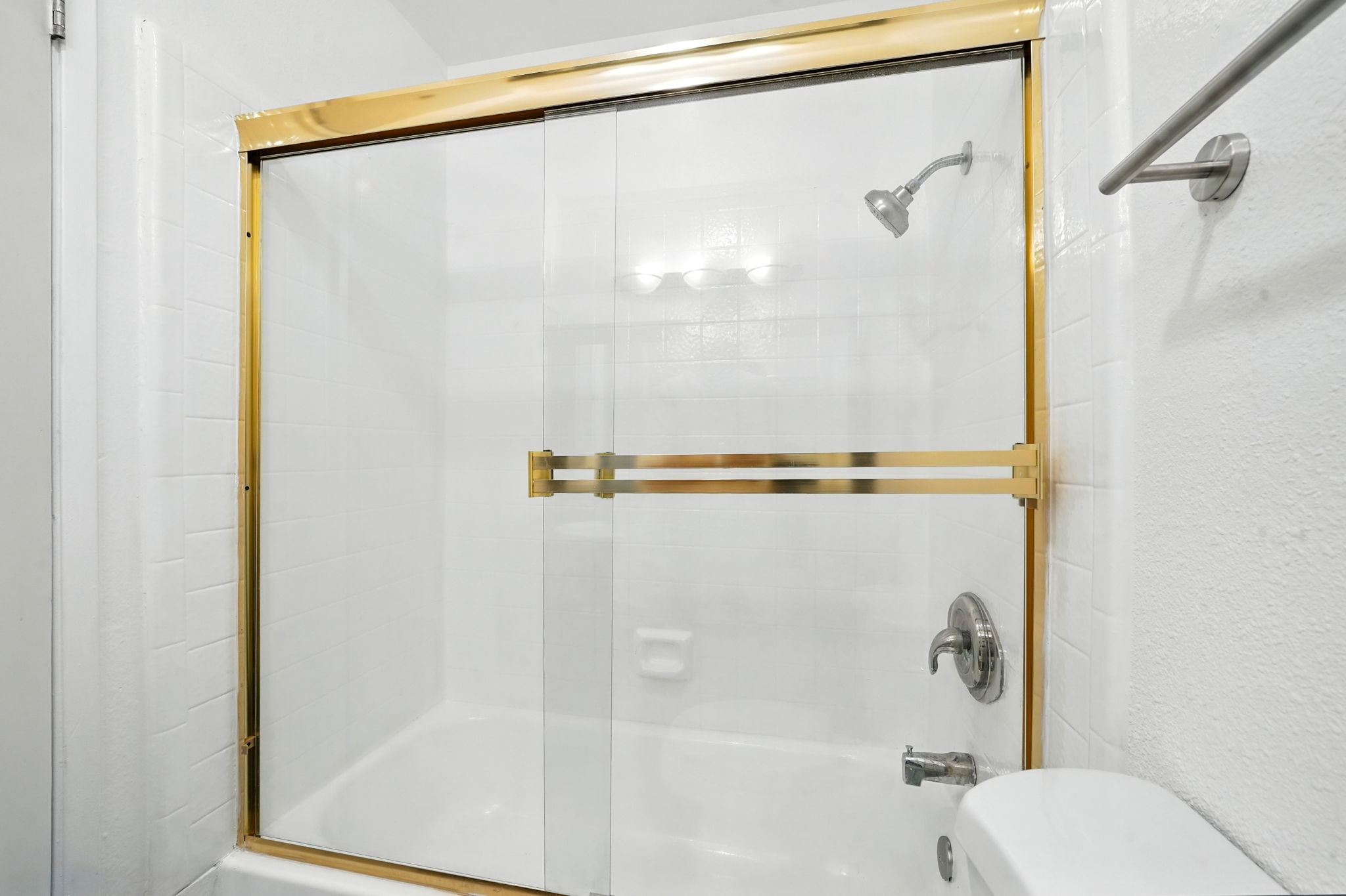 A white bathroom with a gold shower door.