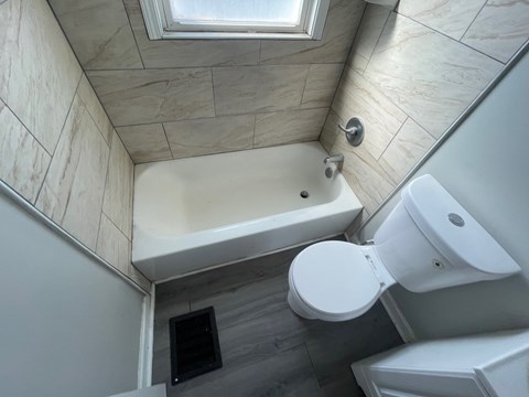 A bathroom with a white toilet and a bathtub with a skylight above it.