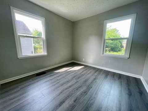 A room with grey walls and wooden flooring with two windows.