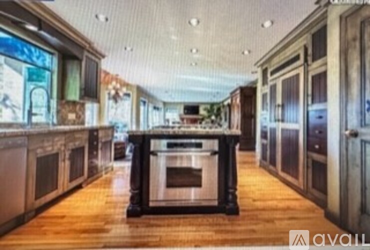 A kitchen with wooden floors and a central island with a stove top oven.
