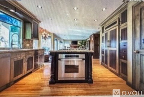A kitchen with wooden floors and a central island with a stove top oven.