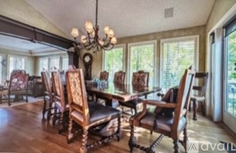 A dining room with a chandelier, wooden chairs, and a table.