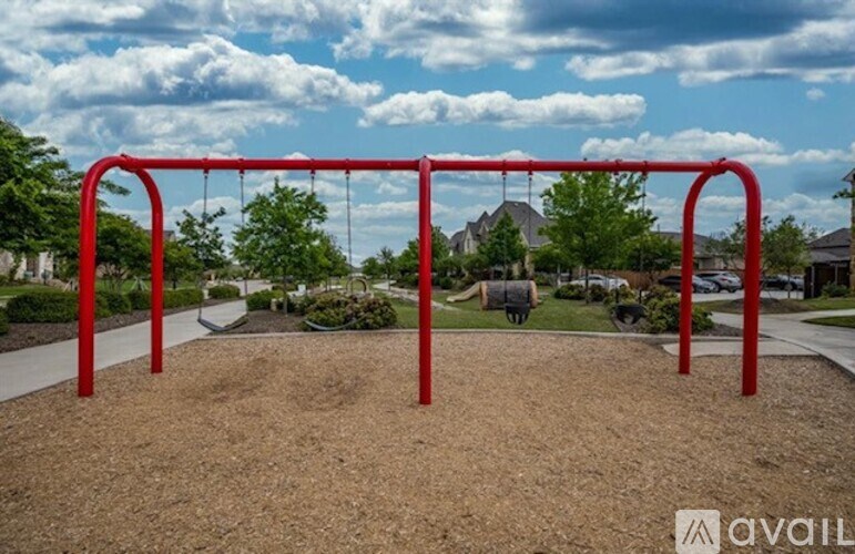 A red swing set in a playground surrounded by a gravel area.