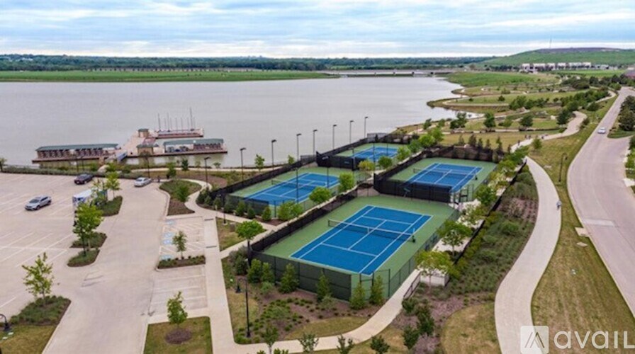 A tennis court is surrounded by a parking lot and a body of water.