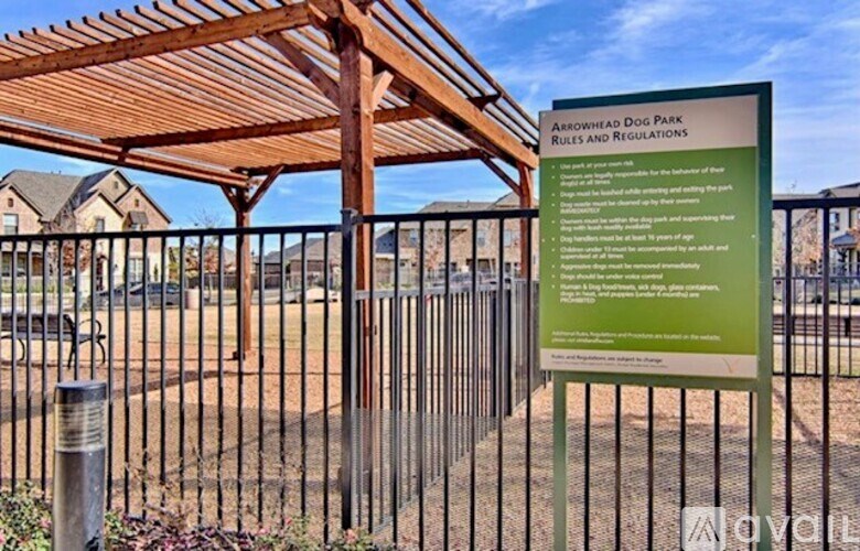 A sign for Arrowhead Dog Park rules and regulations stands in front of a fence.