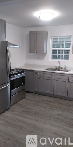 A kitchen with a stainless steel refrigerator and a window with blinds.