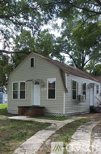 A small house with a white door and windows is surrounded by trees.