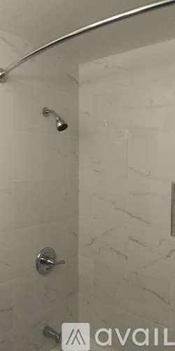 A shower area with a silver shower head and a silver door handle.