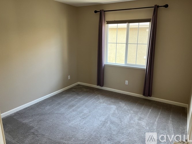 A room with a carpeted floor and a window with curtains.