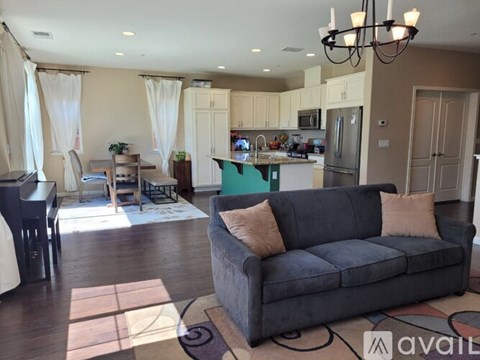 A living room with a grey couch and a kitchen in the background.