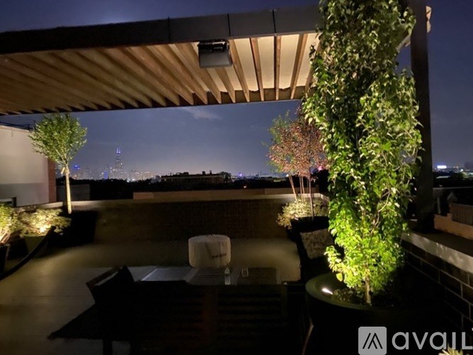 A patio with a table and chairs under a roof with a view of the city at night.