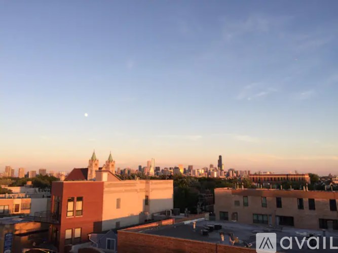 A cityscape at dusk with a clear sky and a moon visible.