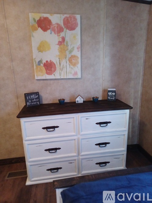 A white chest of drawers with a brown top and a painting of flowers on the wall.