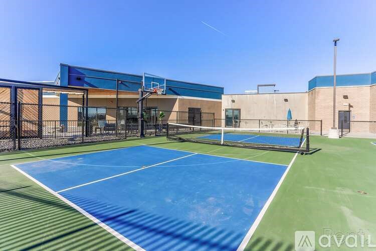 A tennis court with a blue surface and white lines is surrounded by a black fence.