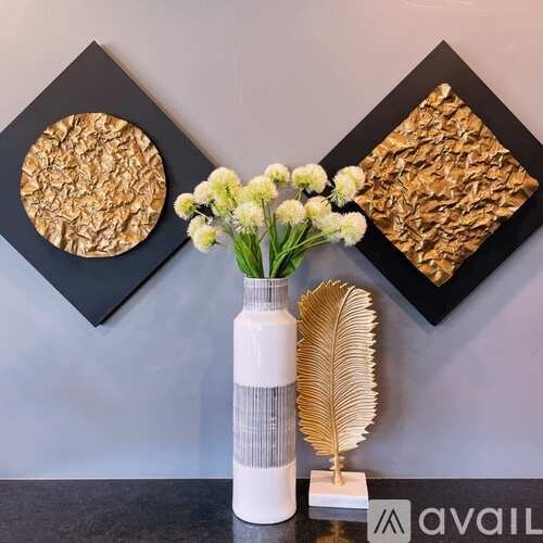 A white vase with flowers sits on a table in front of two framed artworks.