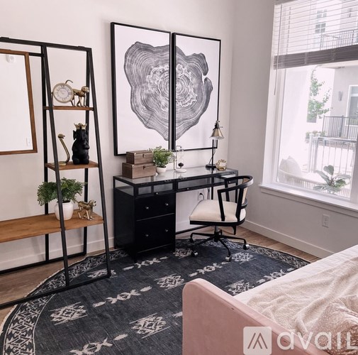 A black and white abstract art piece hangs on a wall above a black desk with a white chair.