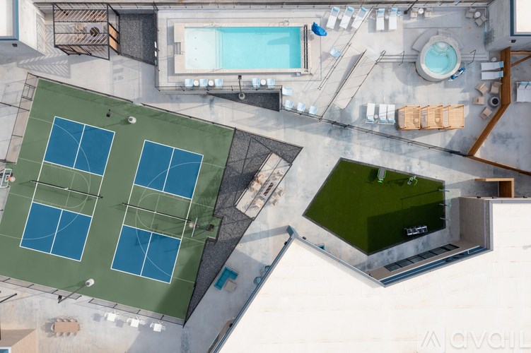 A tennis court is surrounded by a pool and a green area.
