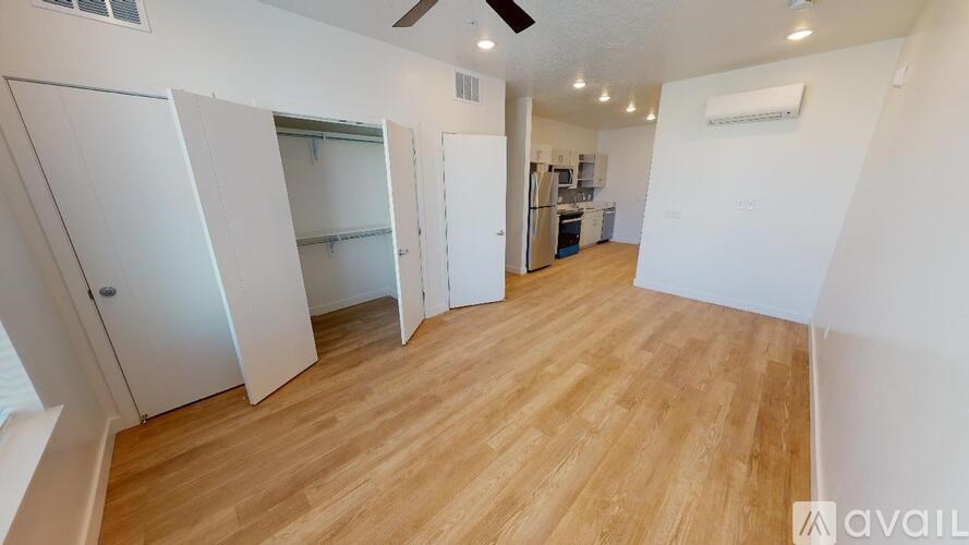 A room with wooden flooring and white walls, featuring a kitchen area with a refrigerator, a sink, and a stove.