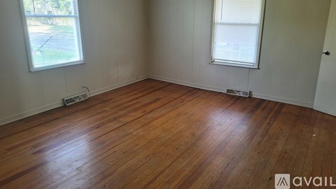 A room with wooden flooring and two windows.