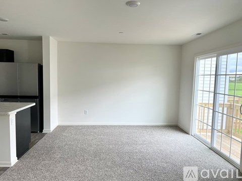 A spacious living room with a grey carpet and a large window overlooking a balcony.