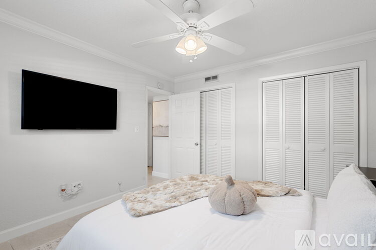 A bedroom with a white bed and a black television mounted on the wall.