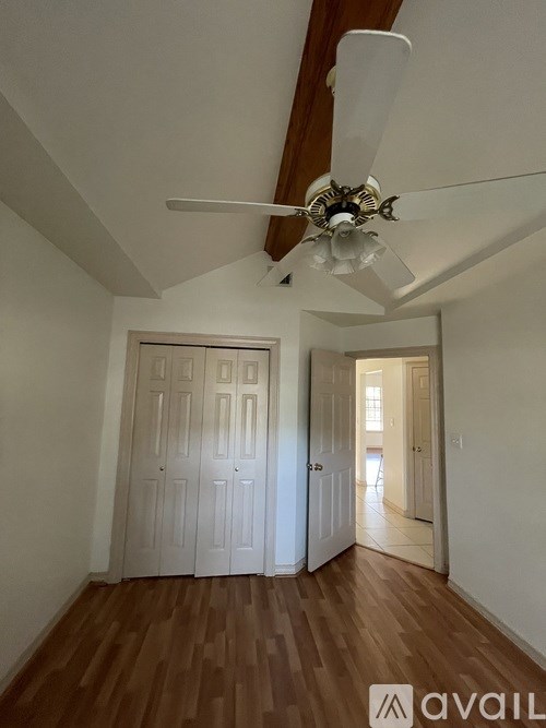 A room with a fan and wooden floors.