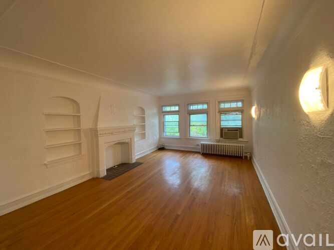 A room with wooden floors and white walls, featuring a fireplace and a window with a view of the sky.