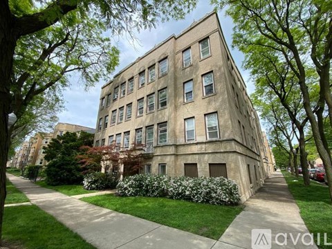 A tall building with many windows is surrounded by trees and greenery.