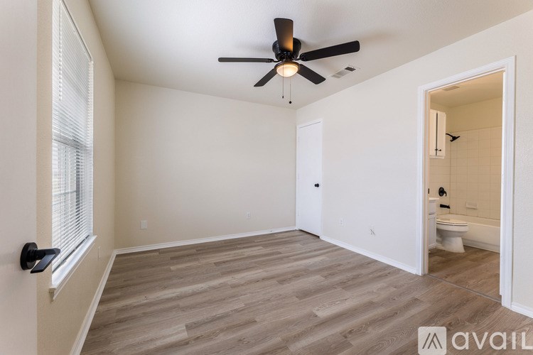 A room with a ceiling fan and light, a window with blinds, and a door leading to a bathroom.