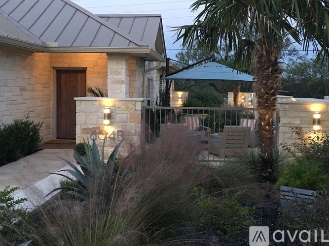 A house with a stone facade and a brown door is surrounded by plants and trees.