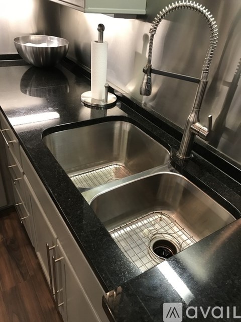 A modern kitchen sink with a chrome faucet and a black countertop.