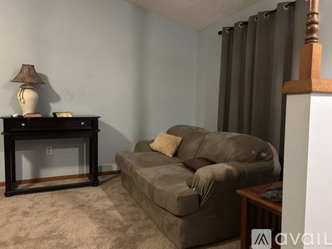 A brown couch sits in a living room with a lamp and a table nearby.