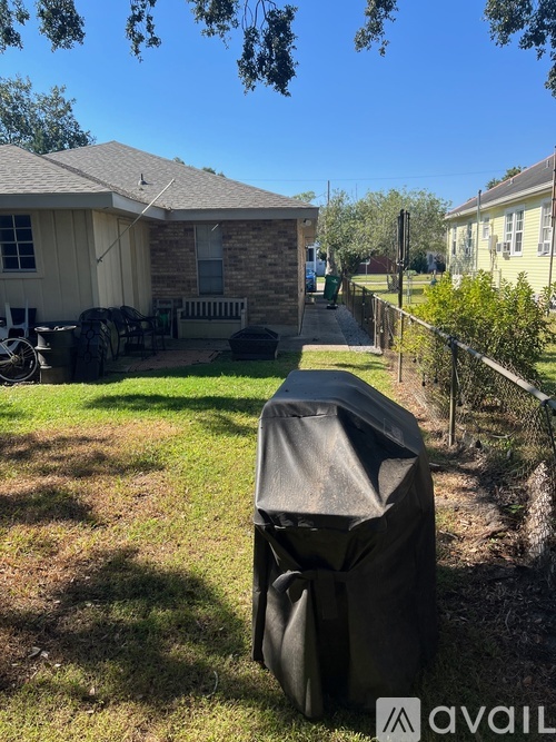 A covered grill is in the foreground of a sunny backyard.