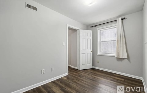 A white door is on the left of a room with a wooden floor.