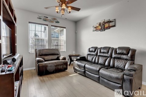 A living room with a brown leather couch and a ceiling fan.
